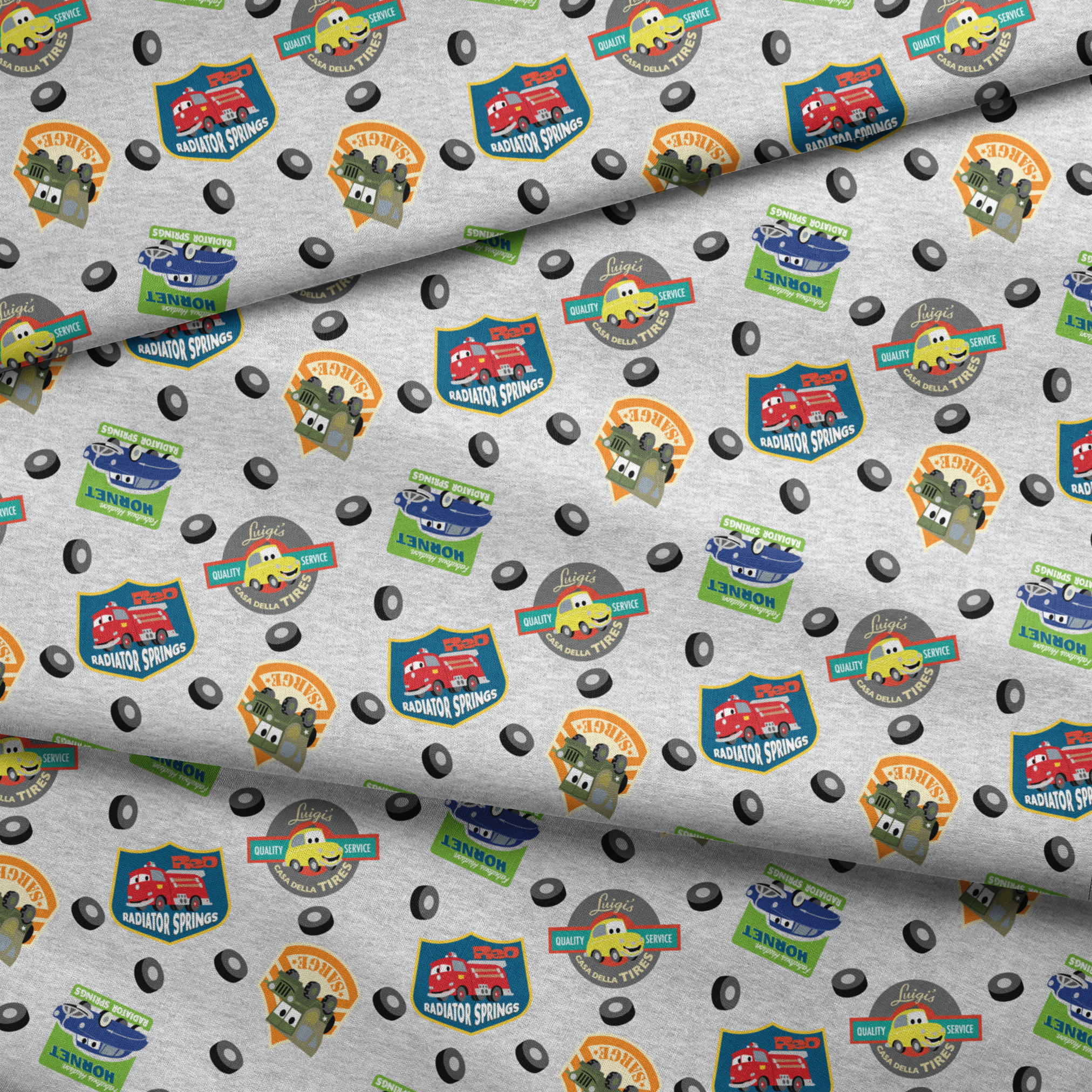 Cartoon vehicle characters on gray fabric with badges for Radiator Springs, Luigi's, and Sarge's fabric fold mockup