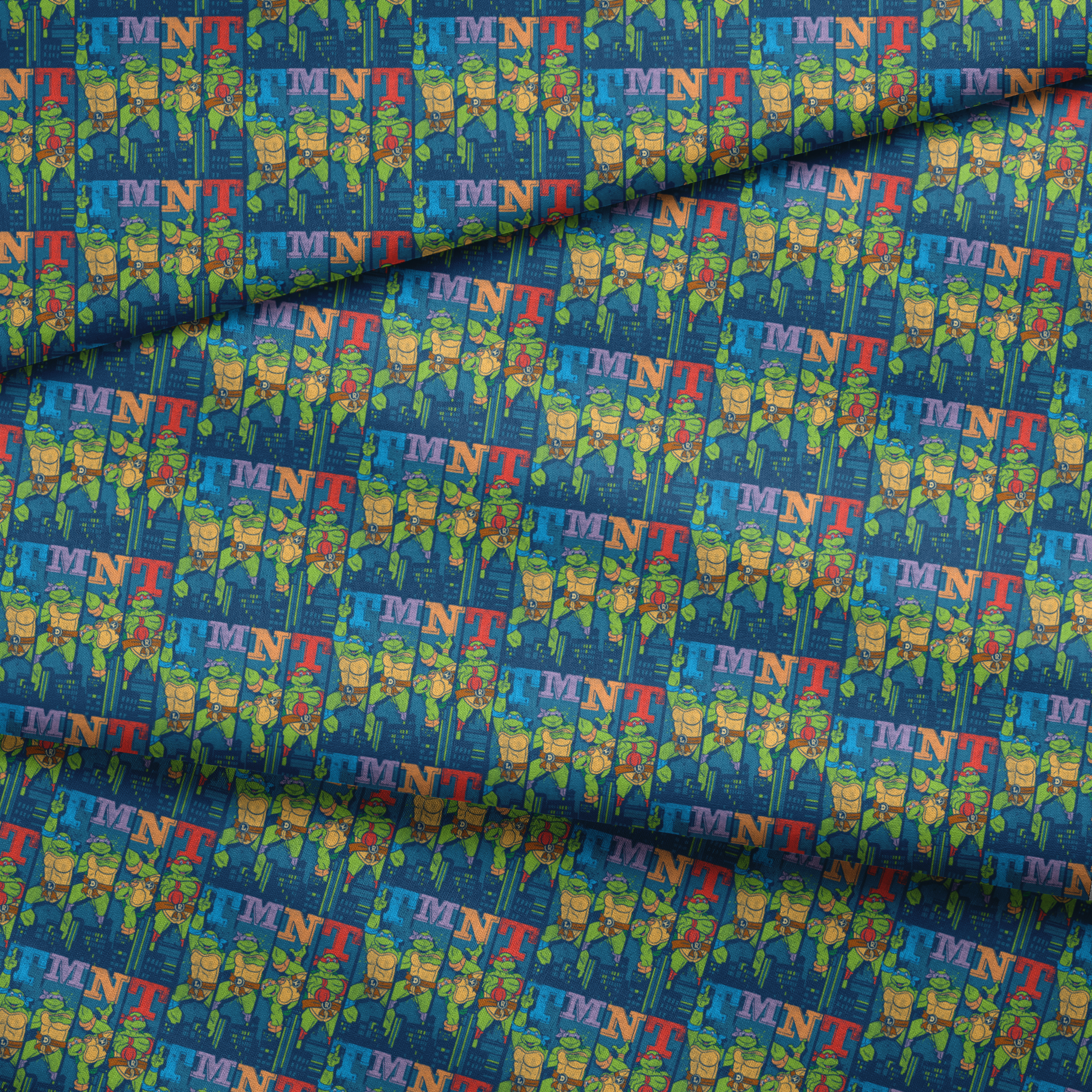 Colorful Teenage Mutant Ninja Turtles cartoon pattern with characters and "TMNT" text on blue cityscape background fabric fold mockup