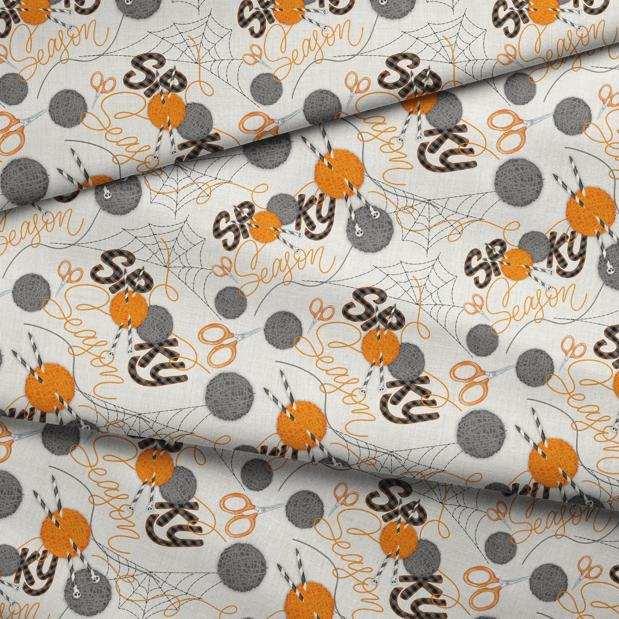 Halloween design by Nicole Tamarin featuring orange and gray yarn balls, scissors, spiderwebs, and “Spooky Season” lettering on a cream background. fabric fold mockup