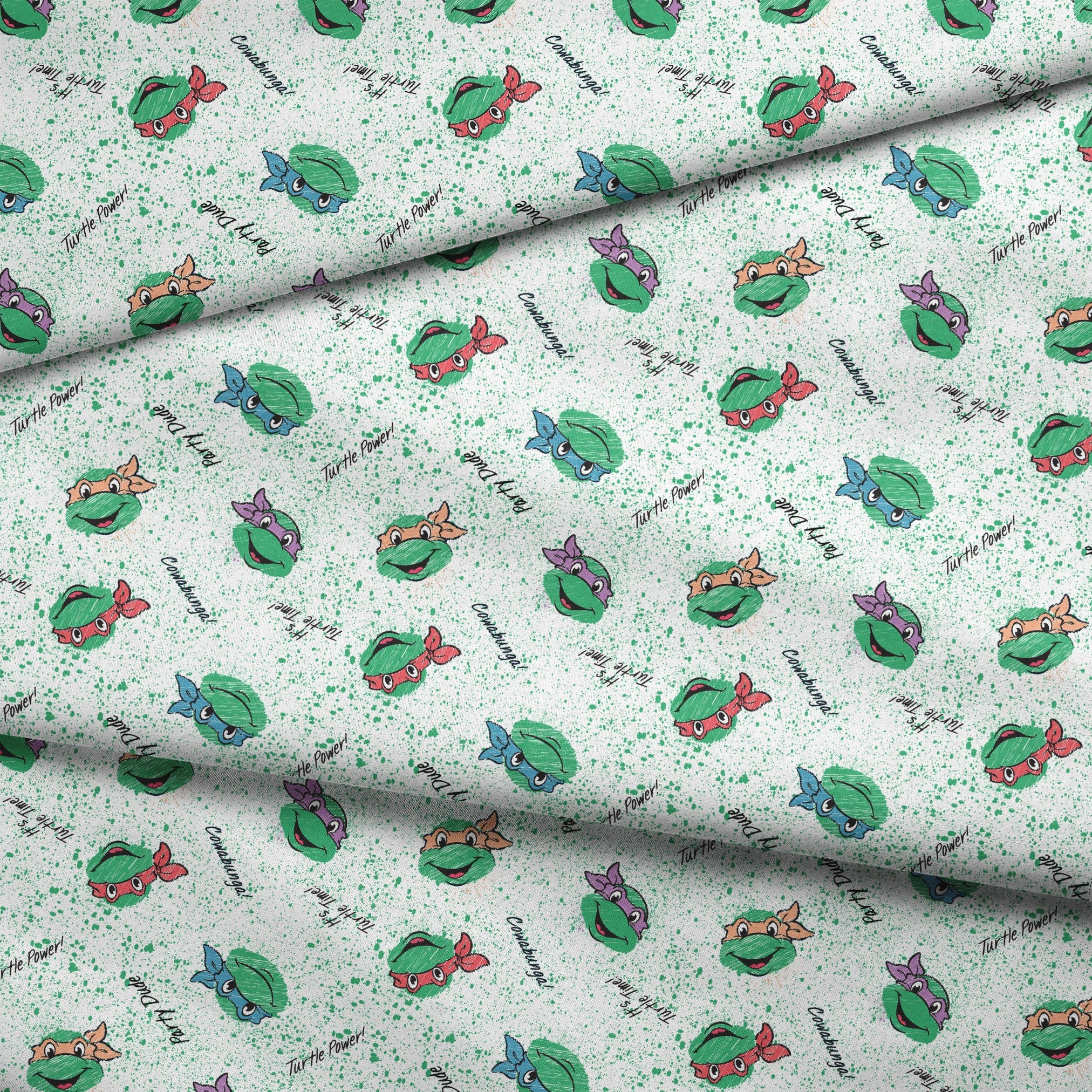 Pattern of Teenage Mutant Ninja Turtles with colorful masks on speckled green background with phrases like "Turtle Power! fabric fold mockup