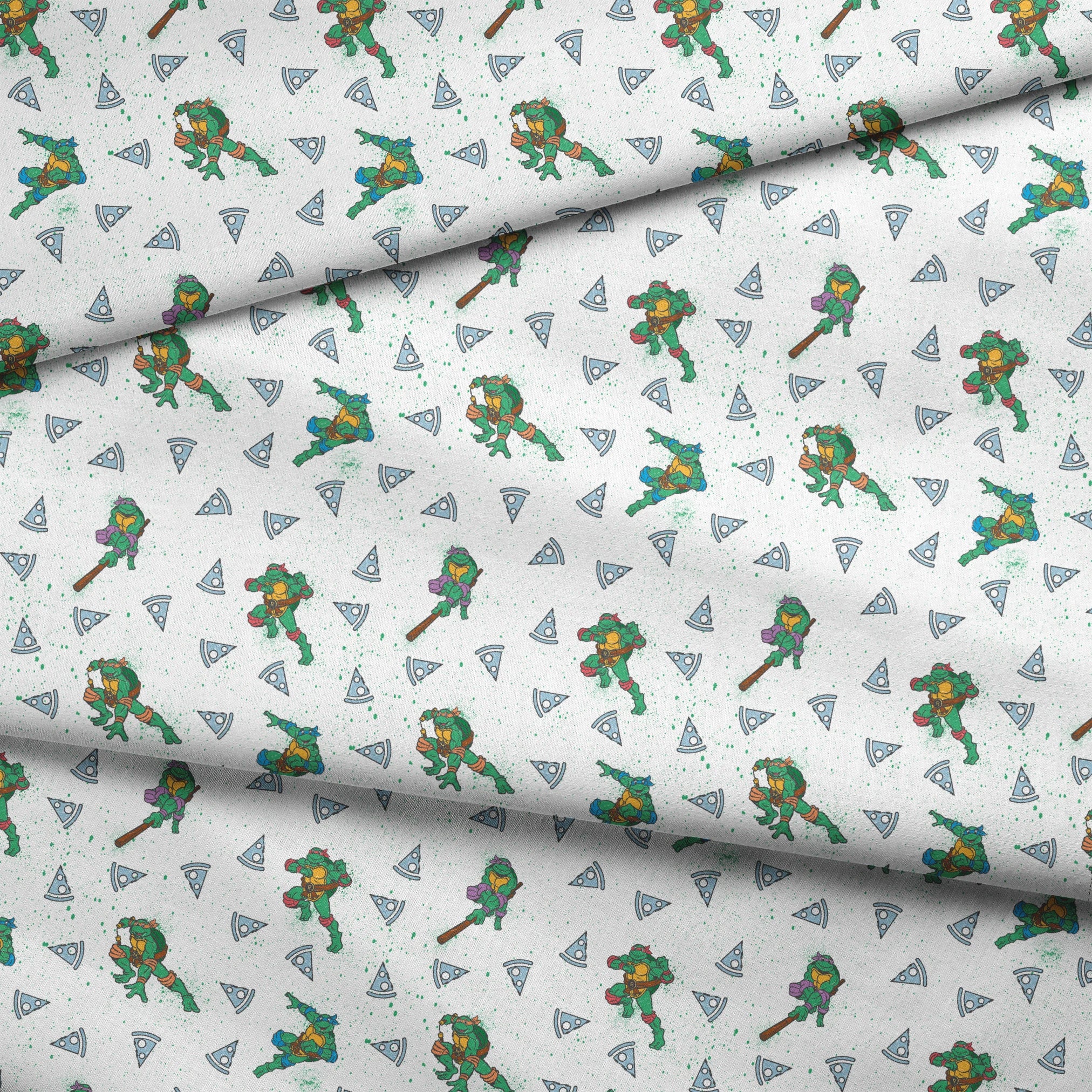 Teenage Mutant Ninja Turtles in action poses scattered among pizza slices on white speckled background fabric fold mockup