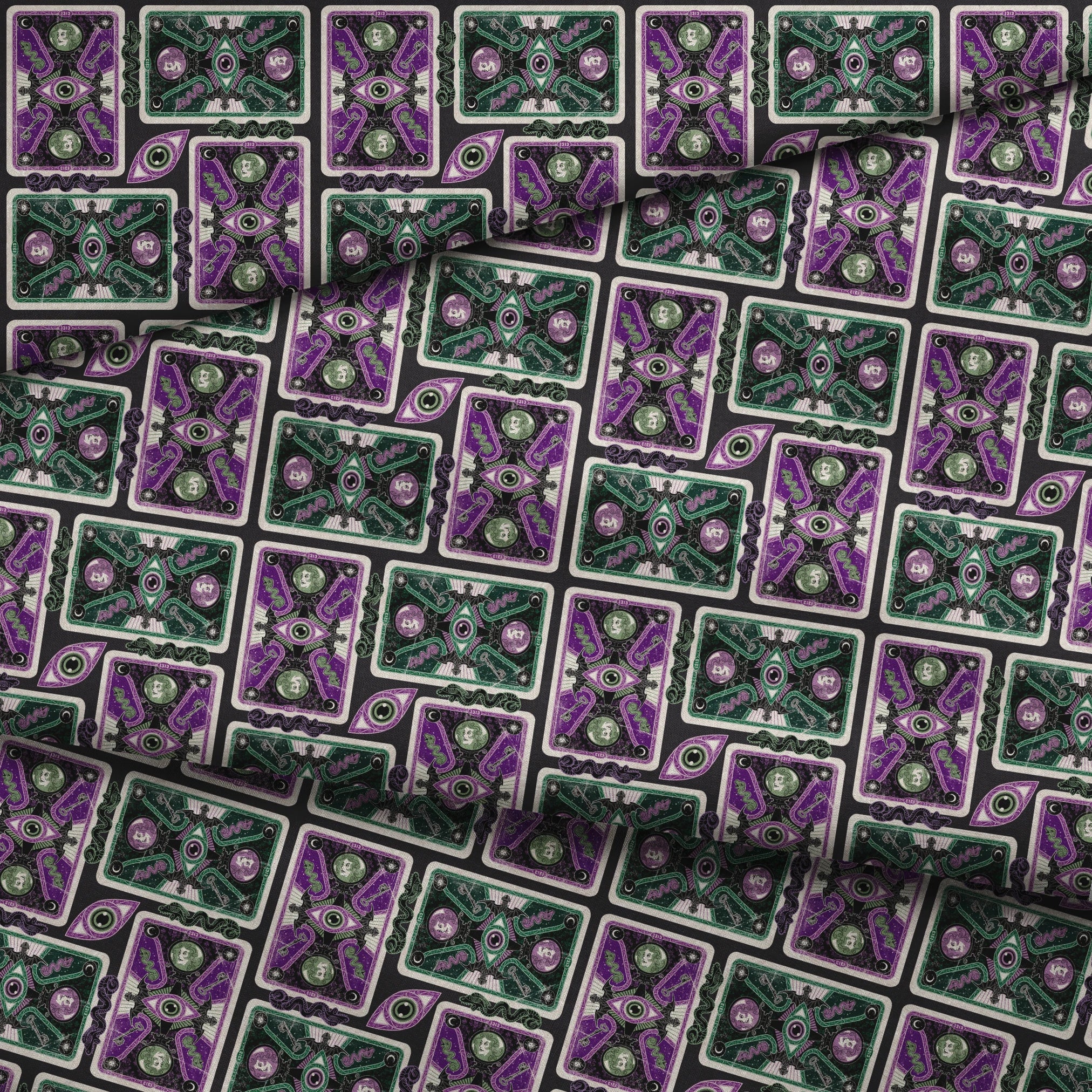 Ornate playing card designs with purple and green patterns featuring central eye motifs and circular number elements against a black background. fabric fold mockup
