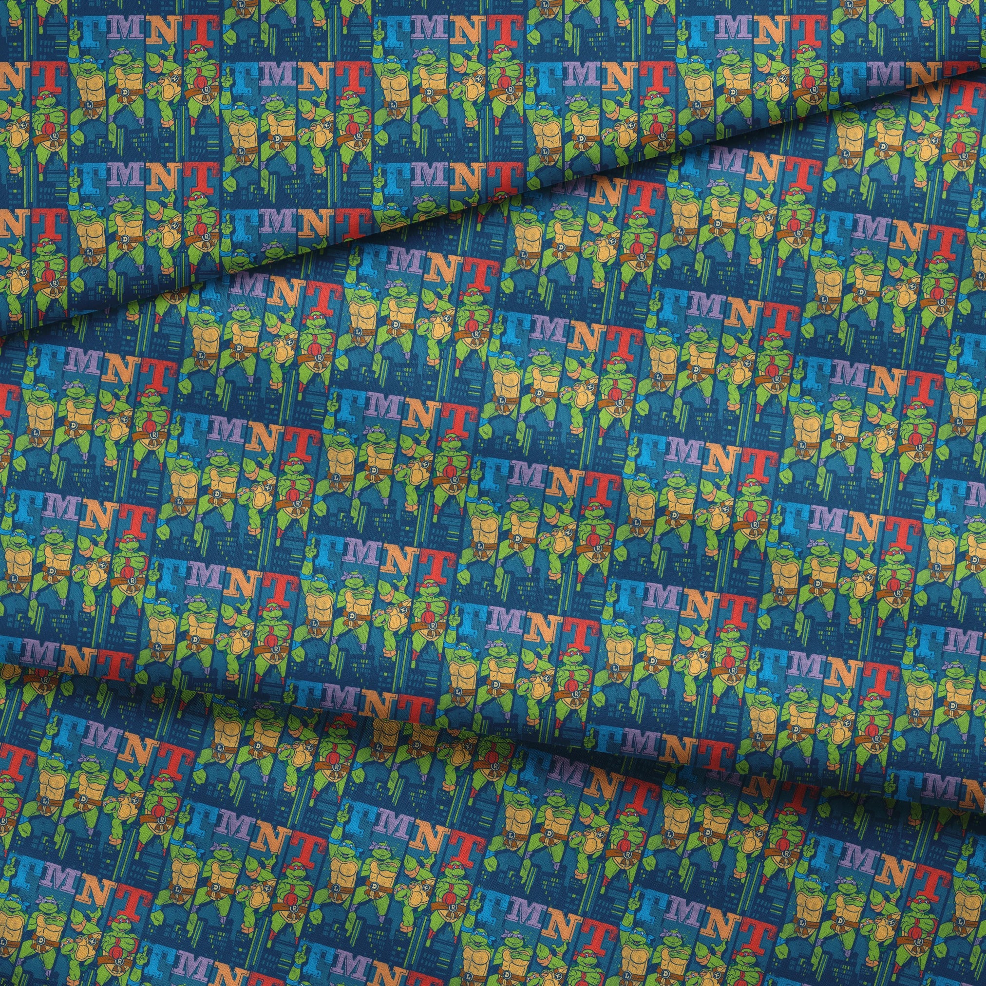 Colorful Teenage Mutant Ninja Turtles cartoon pattern with characters and "TMNT" text on blue cityscape background fabric fold mockup
