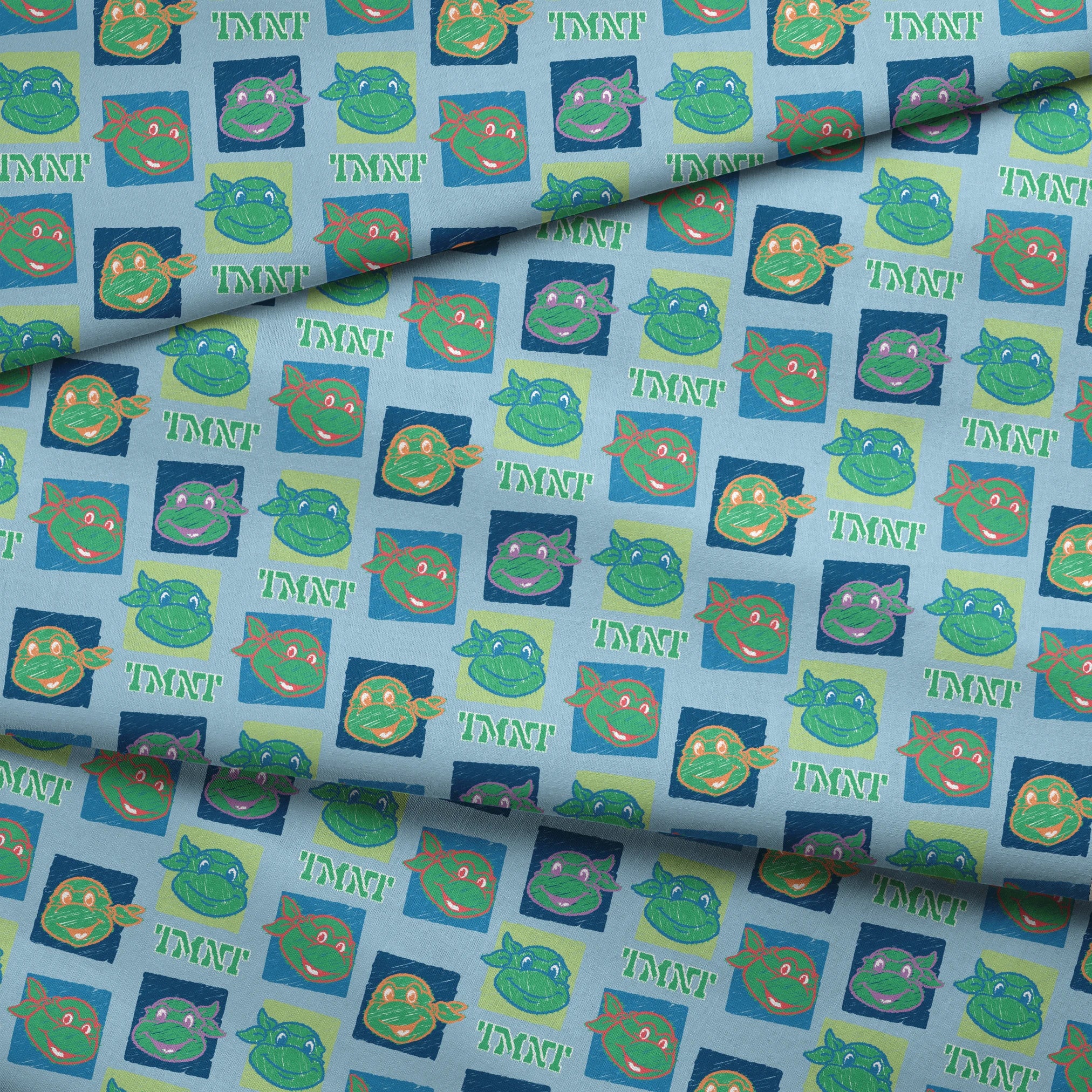 Teenage Mutant Ninja Turtles pattern with cartoon turtle faces in squares on light blue background fabric fold mockup