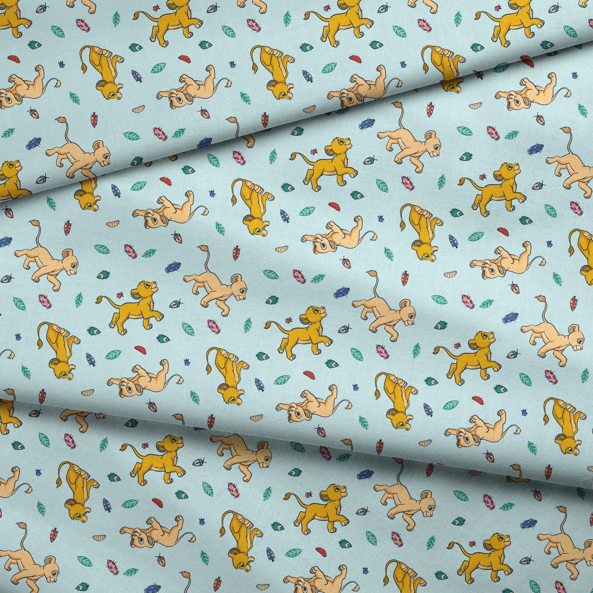 Lion cubs playing on light blue background with colorful leaves and plant elements scattered throughout fabric fold mockup
