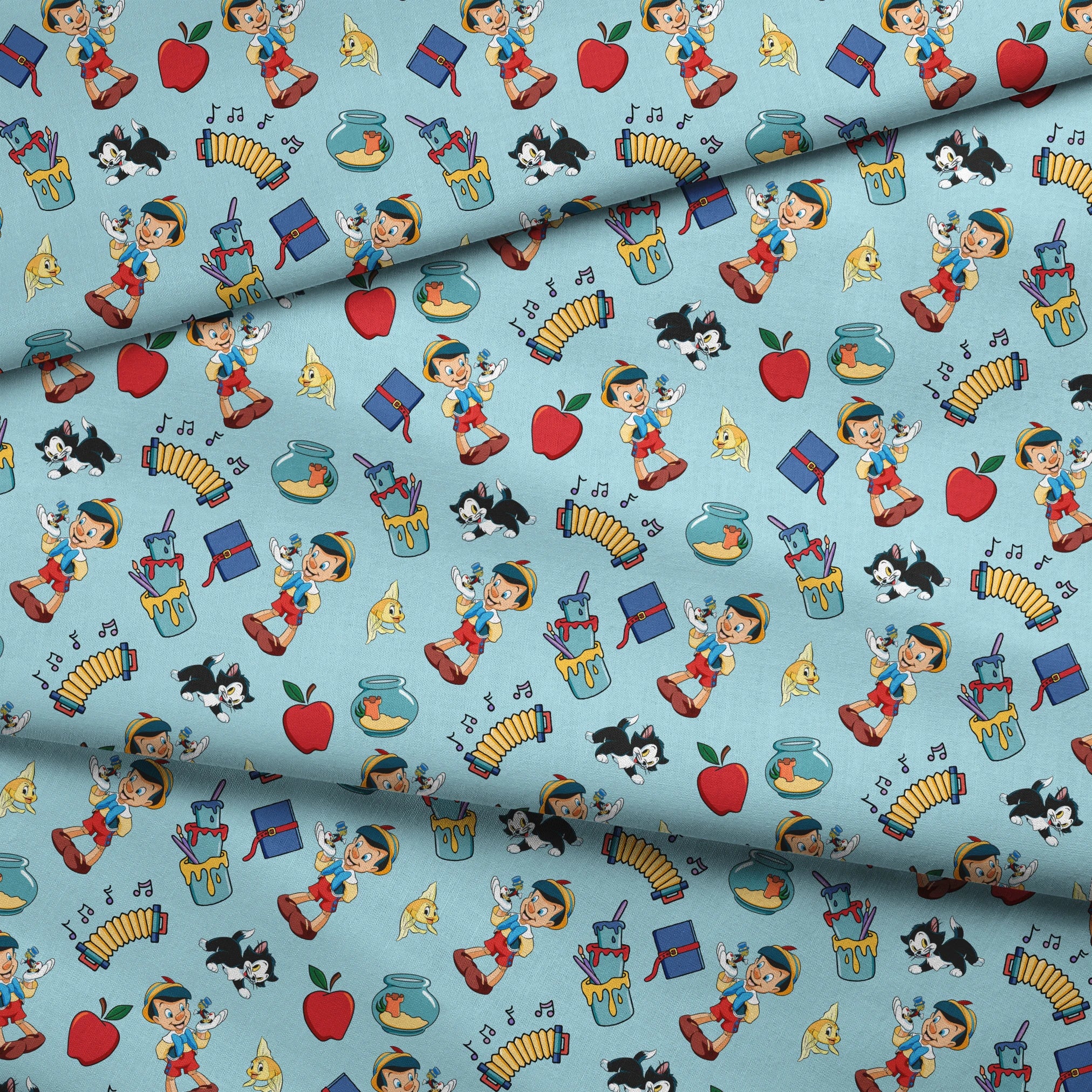 Cartoon pattern with wooden puppets, red apples, musical notes, goldfish bowls, cats, and books on light blue background fabric fold mockup