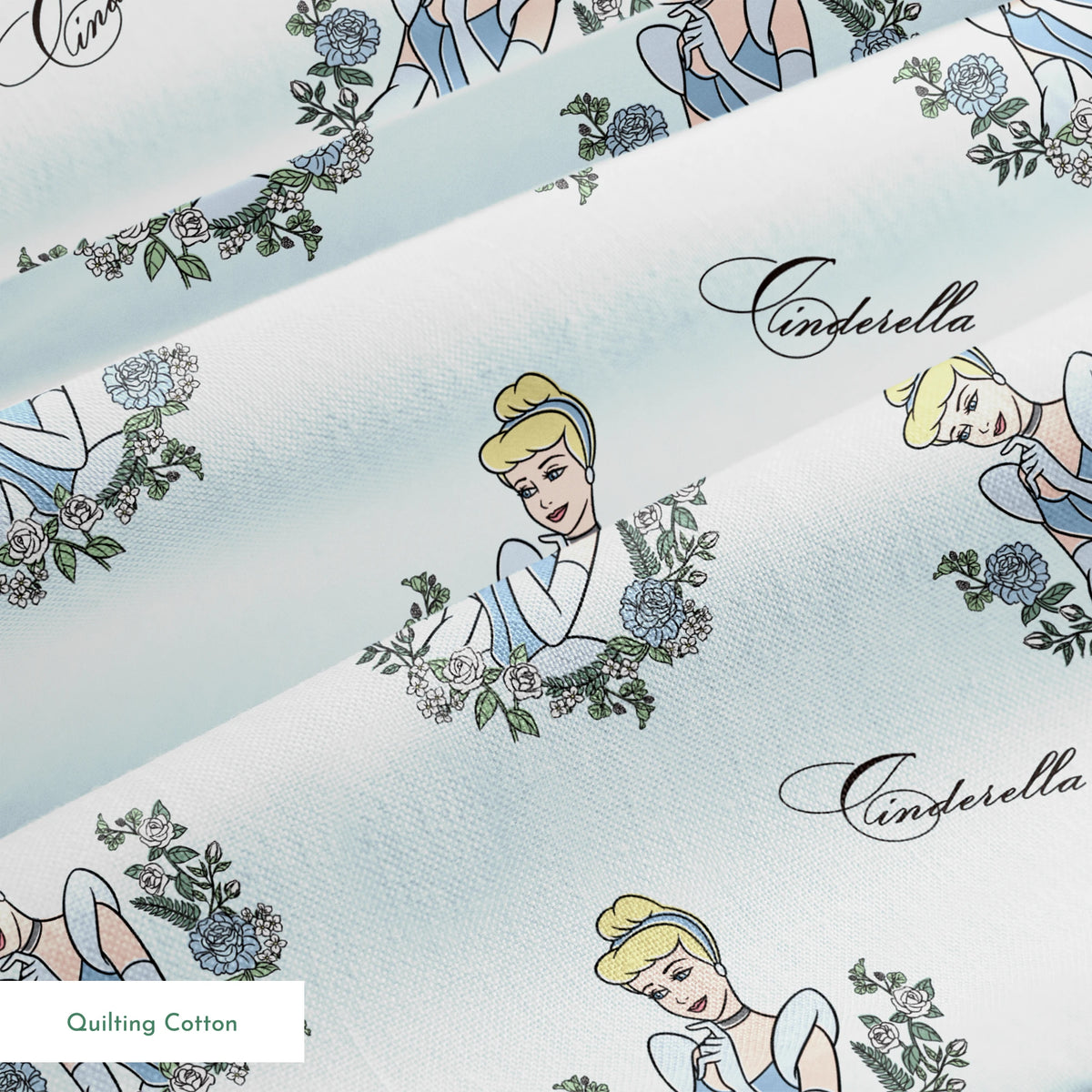 The image shows a pattern featuring a cartoon princess character in a blue dress surrounded by decorative green wreaths on a light blue background. The word "Cinderella" appears in cursive script throughout the design. springs quiltingcotton texture