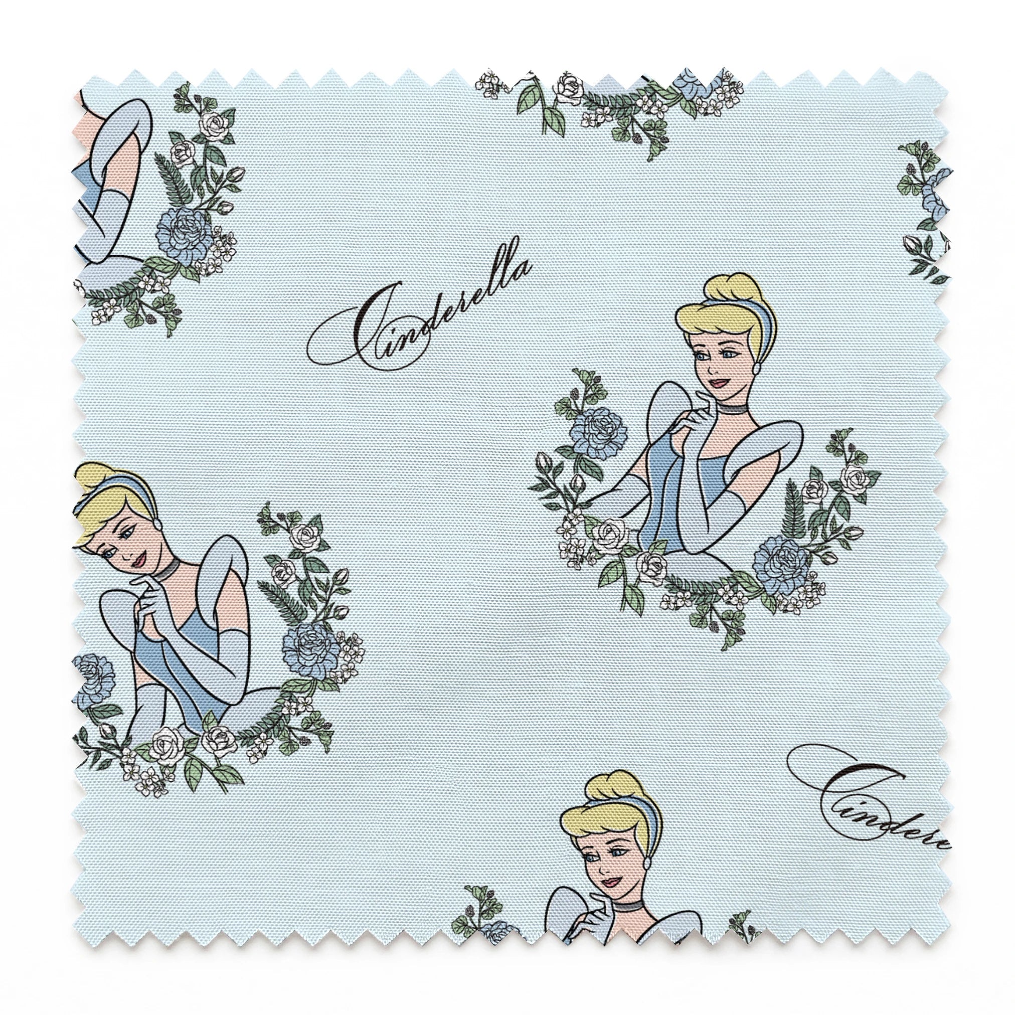 The image shows a pattern featuring a cartoon princess character in a blue dress surrounded by decorative green wreaths on a light blue background. The word "Cinderella" appears in cursive script throughout the design. springs swatch pinked
