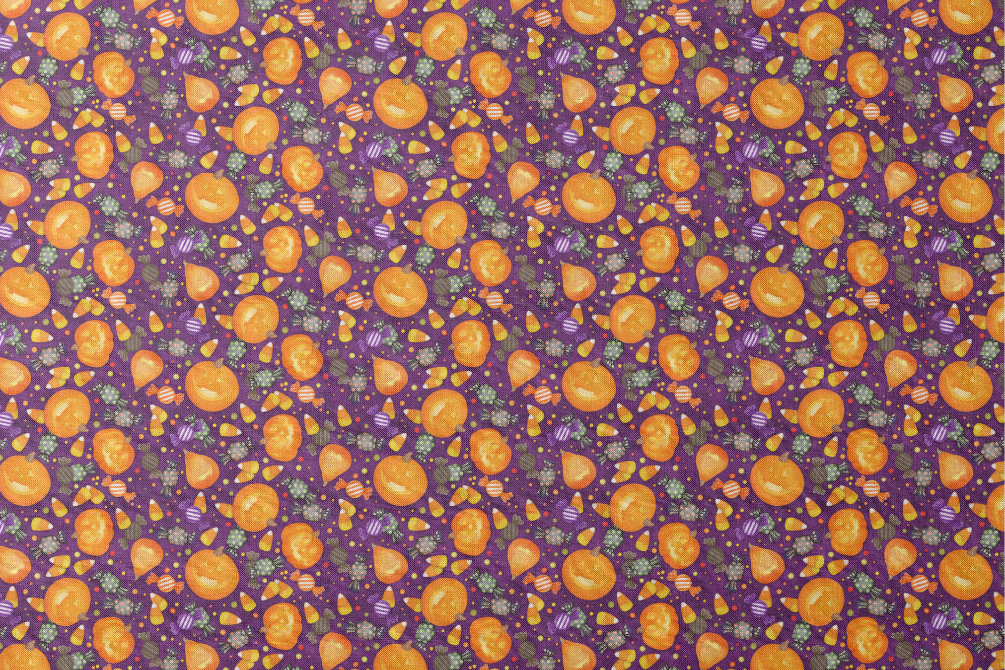 Playful Halloween fabric design by Nicole Tamarin featuring smiling jack-o’-lanterns, wrapped candies, and candy corn scattered across a purple background. designs flat mockup