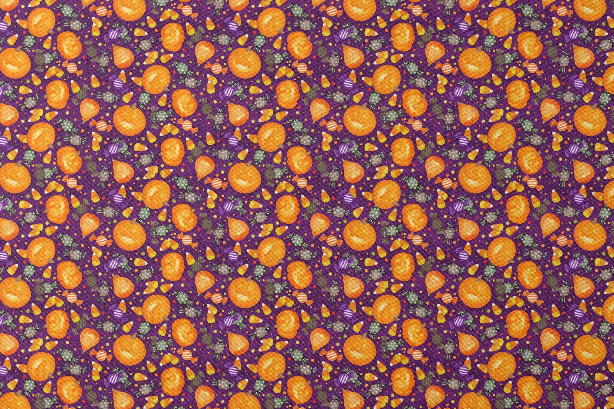 Playful Halloween fabric design by Nicole Tamarin featuring smiling jack-o’-lanterns, wrapped candies, and candy corn scattered across a purple background. designs flat mockup