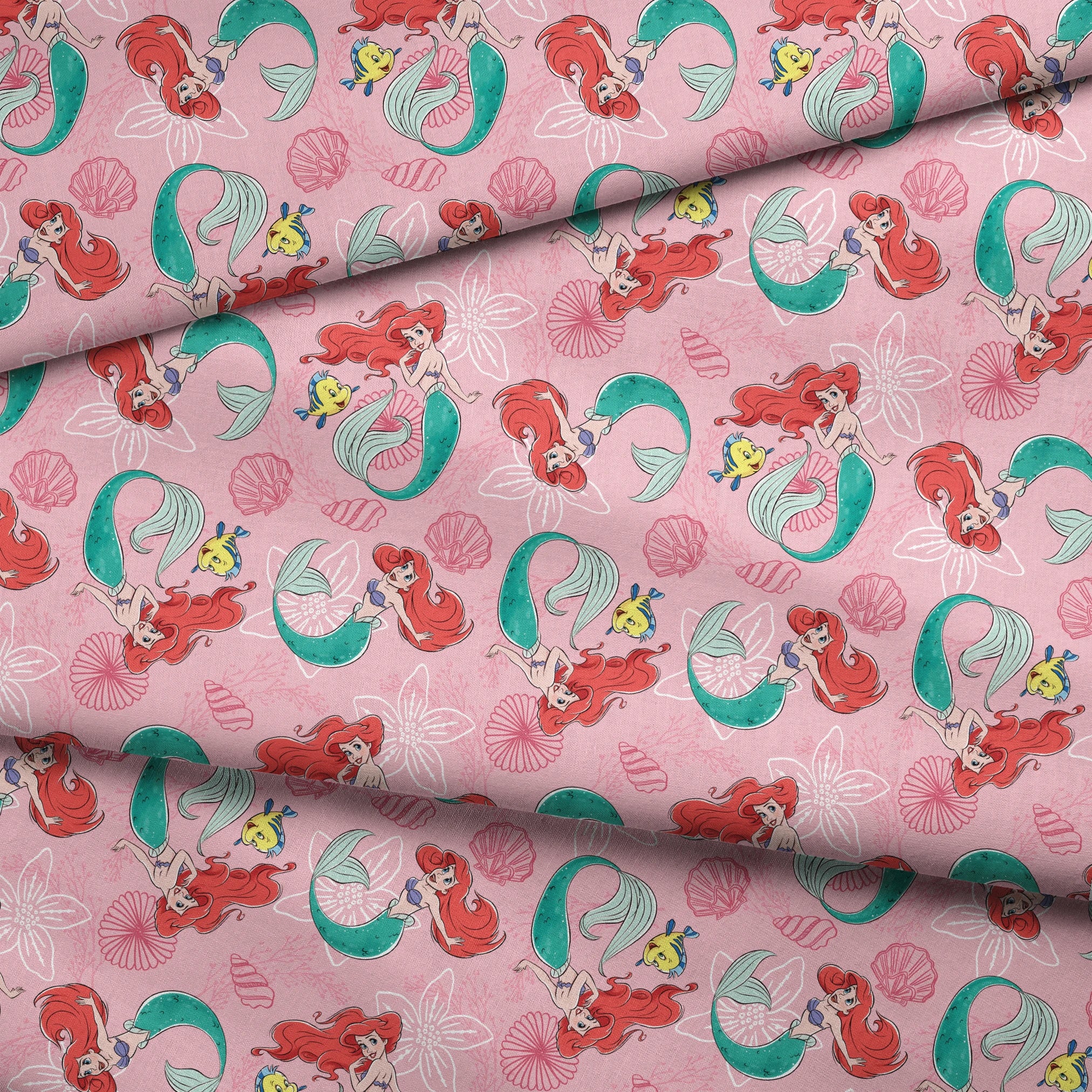 Illustrated pattern of mermaids with red hair and green tails swimming with yellow fish on pink seashell background fabric fold mockup