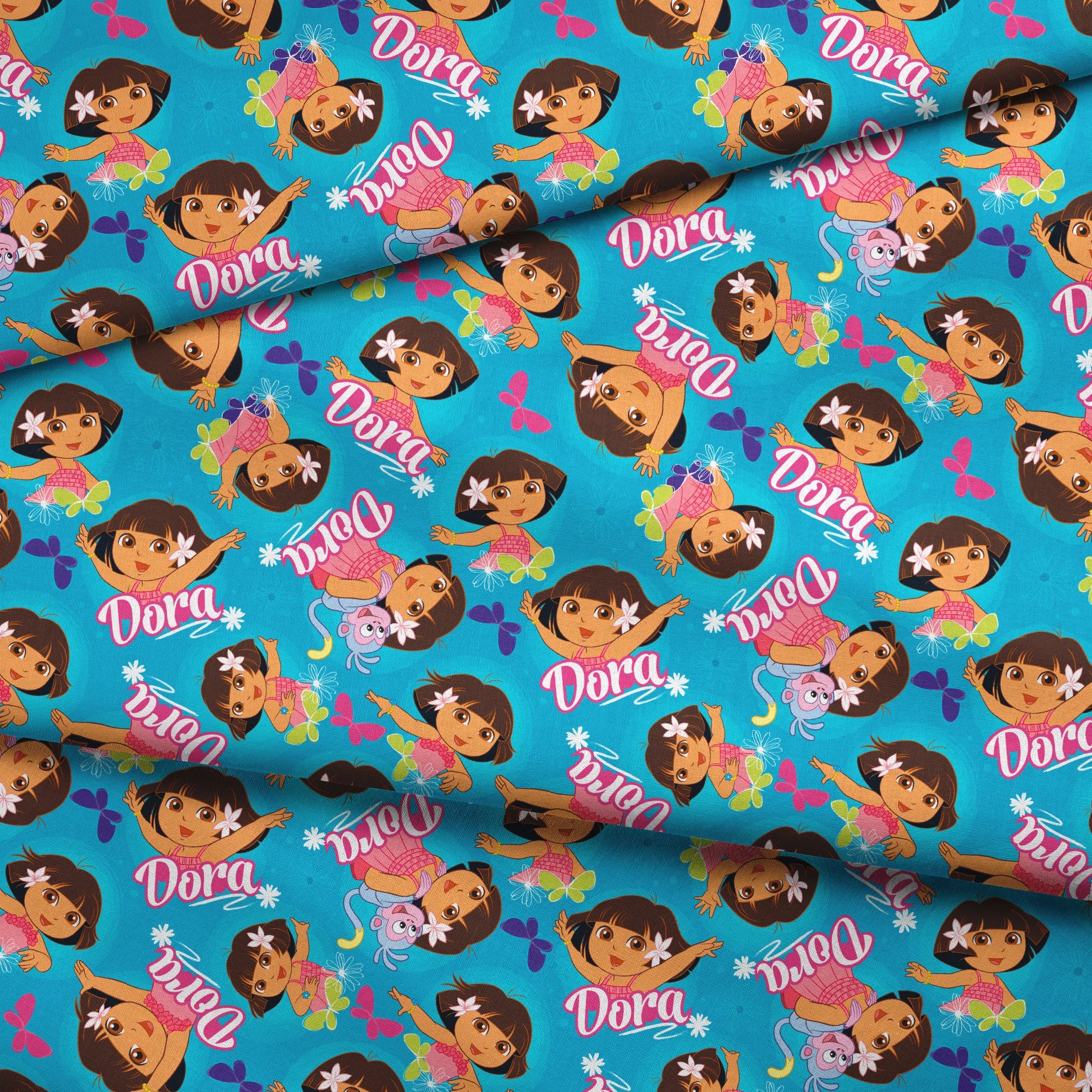Bright blue pattern with cartoon character Dora, flowers, and "Dora" text repeated throughout fabric fold mockup