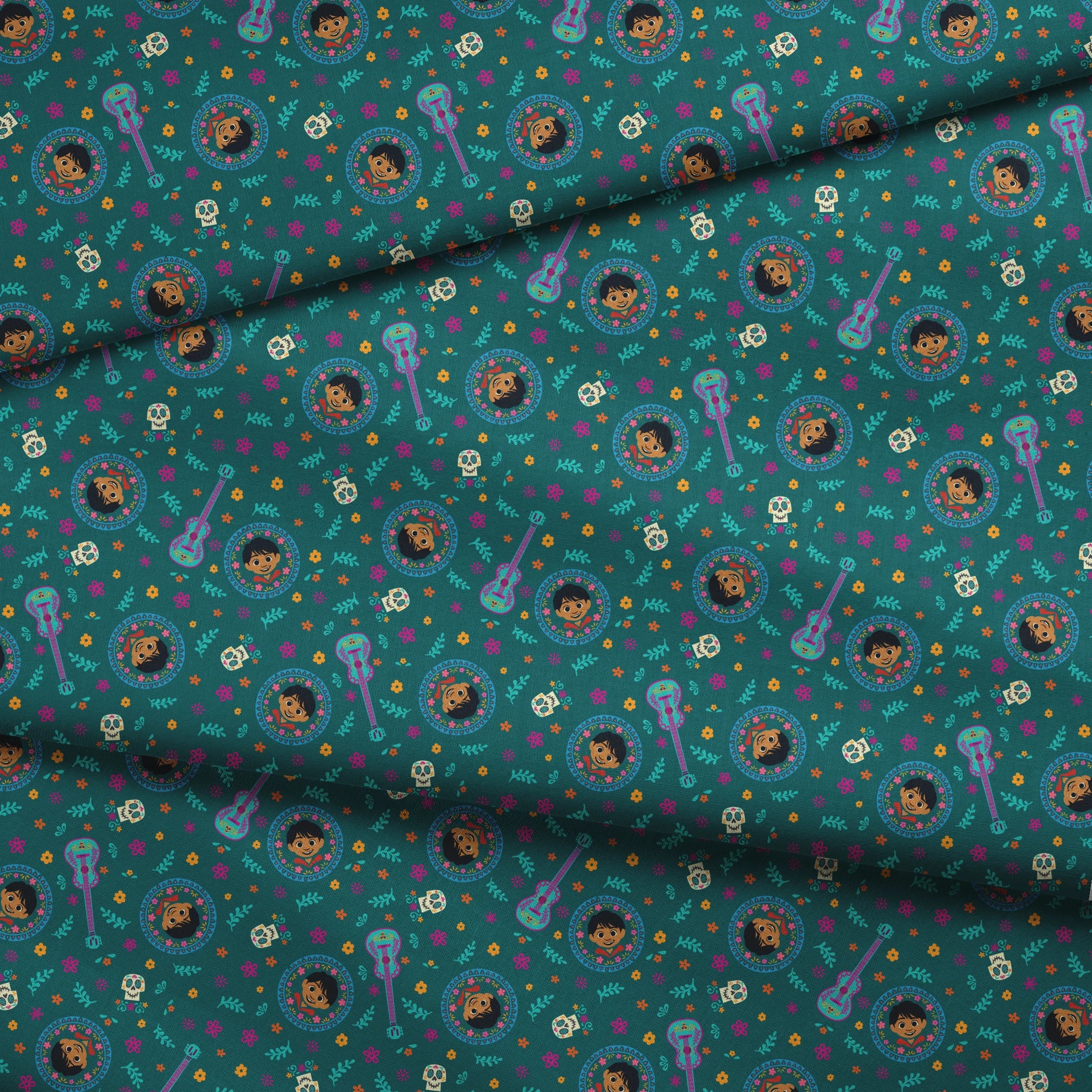Colorful Coco-inspired pattern with guitars, sugar skulls, circular portraits, and floral elements on teal background. fabric fold mockup