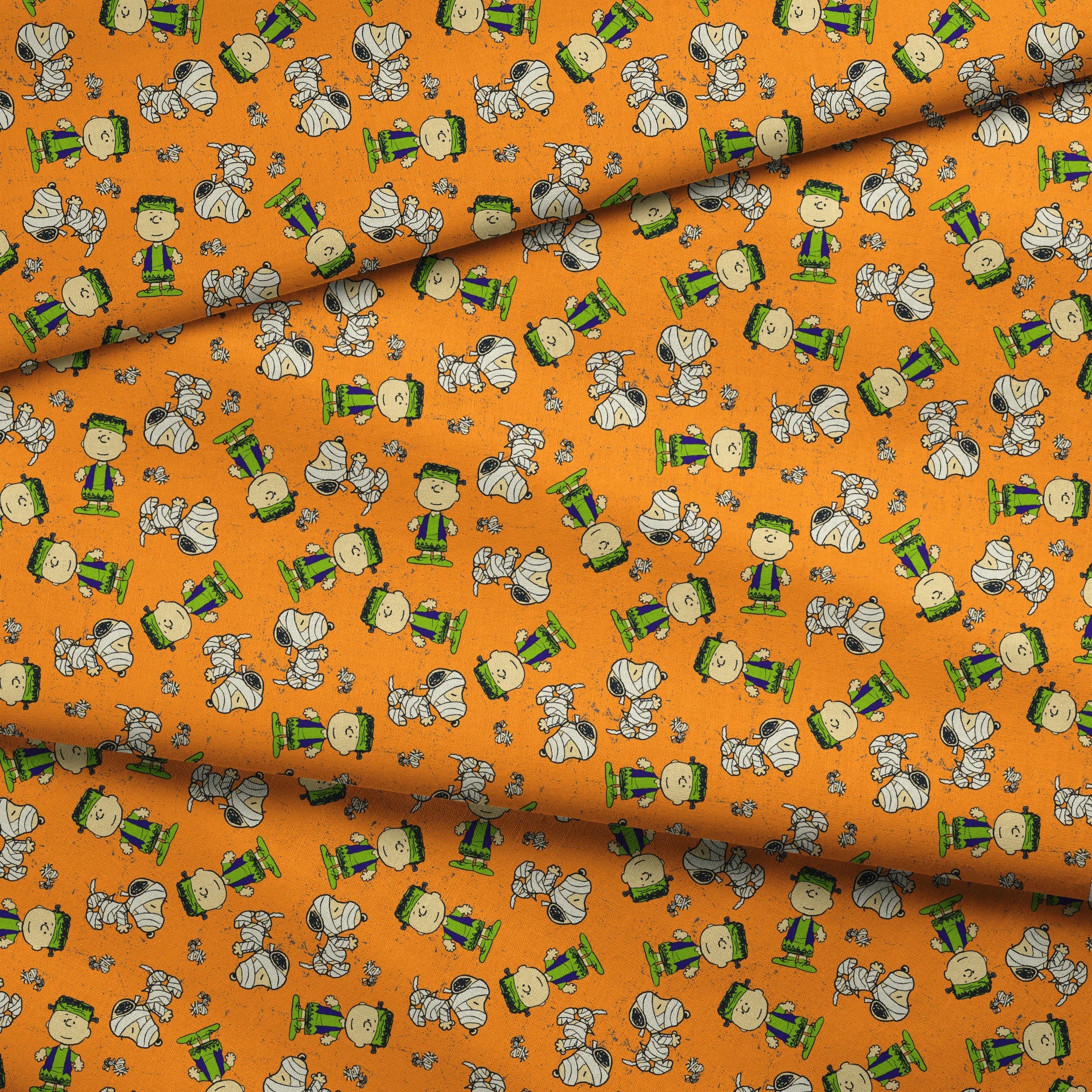 Peanuts characters pattern on orange background with Charlie Brown, Snoopy, and friends scattered throughout fabric fold mockup