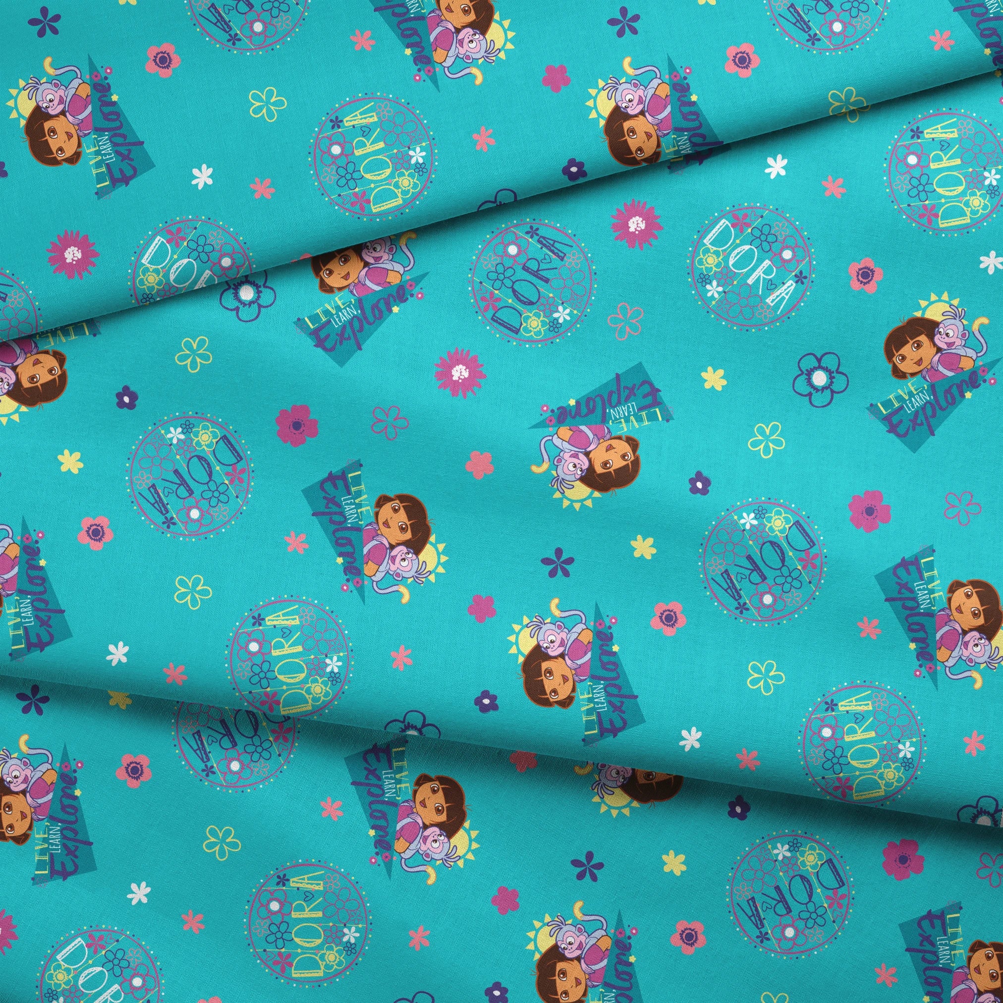 Colorful teal pattern with Dora the Explorer characters, decorative circles, flowers, and triangular shapes in pink, purple, and blue fabric fold mockup