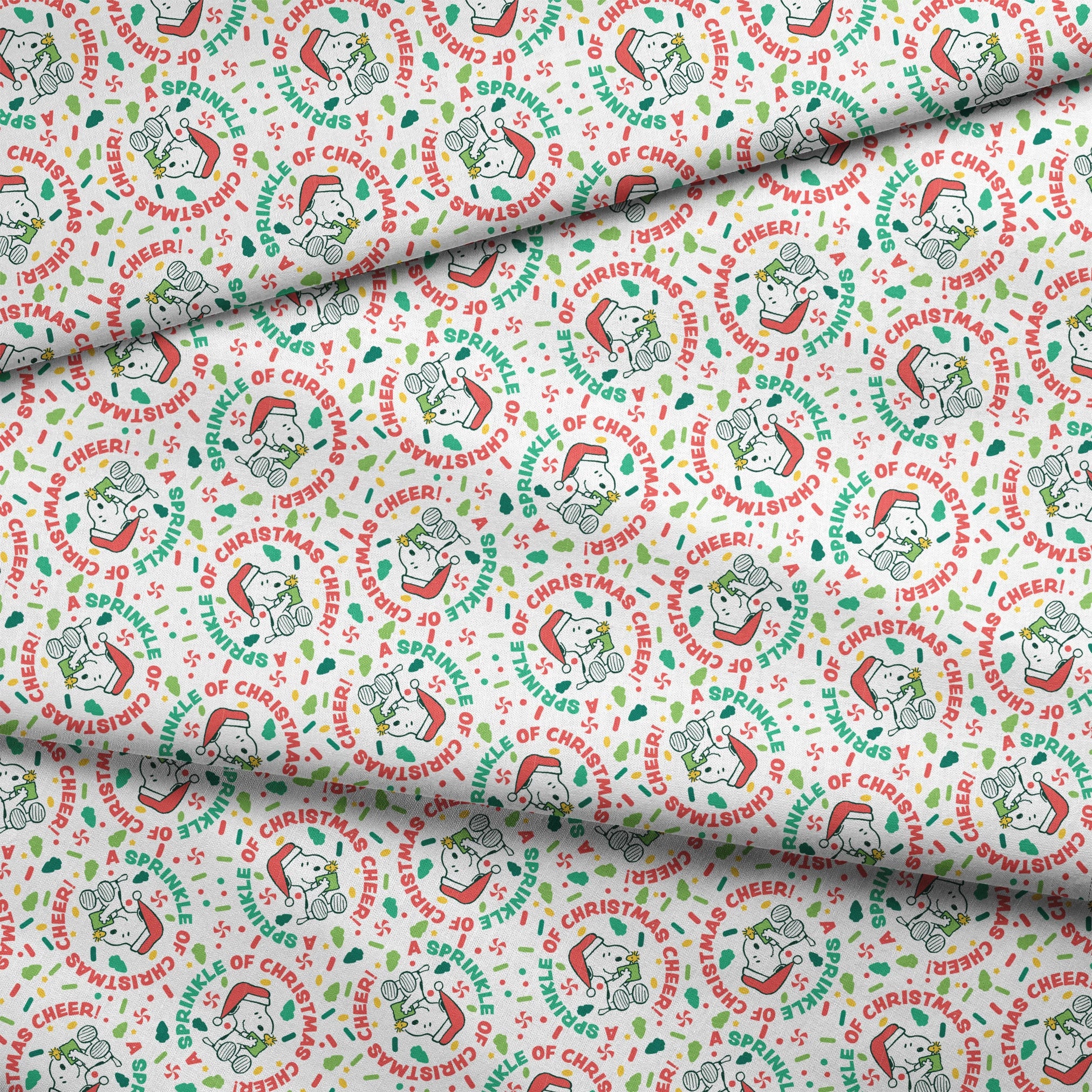 Holiday pattern with Snoopy wearing Santa hat, surrounded by "Merry Christmas", "Cheer", and candy designs on white background fabric fold mockup