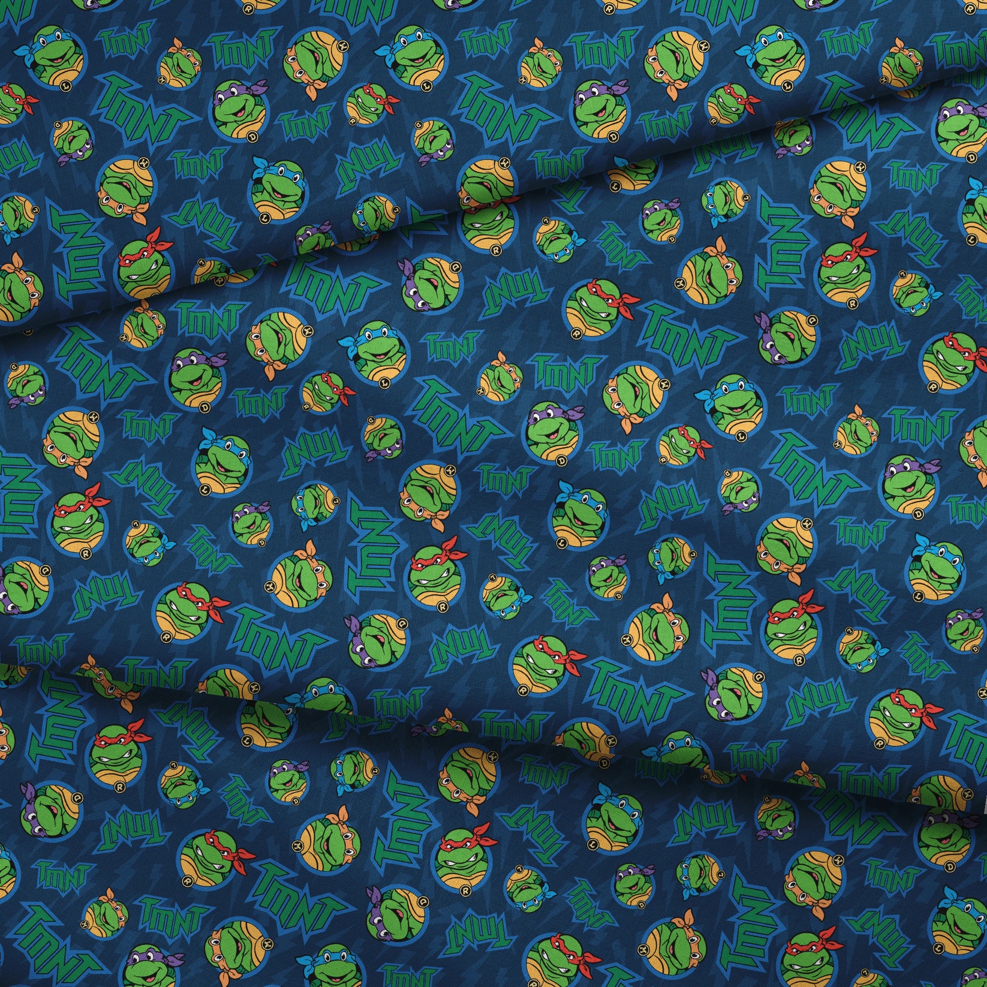 Teenage Mutant Ninja Turtles pattern with character heads and TMNT logos on blue background fabric fold mockup