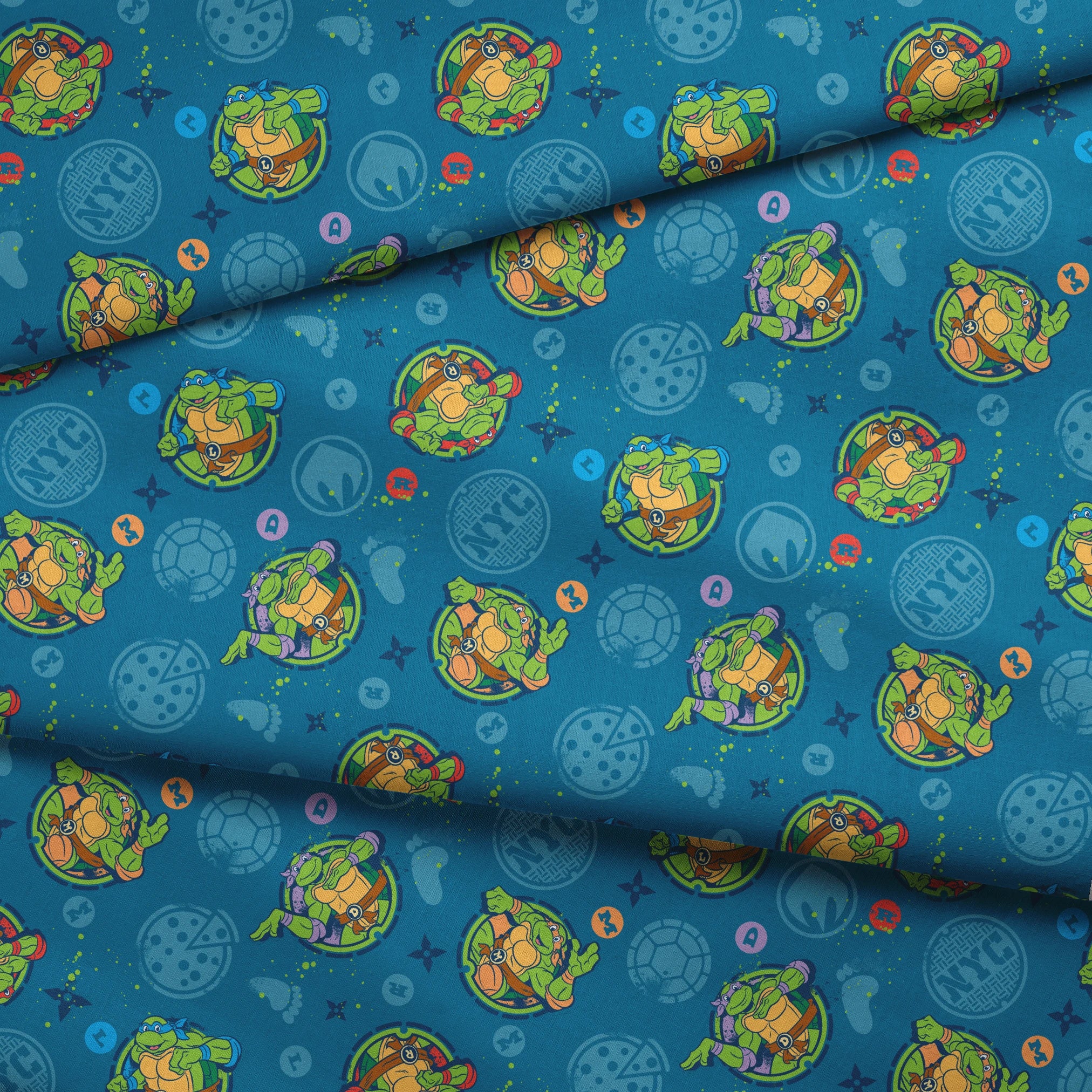 Teenage Mutant Ninja Turtles in circular medallions on teal background with subtle geometric patterns fabric fold mockup