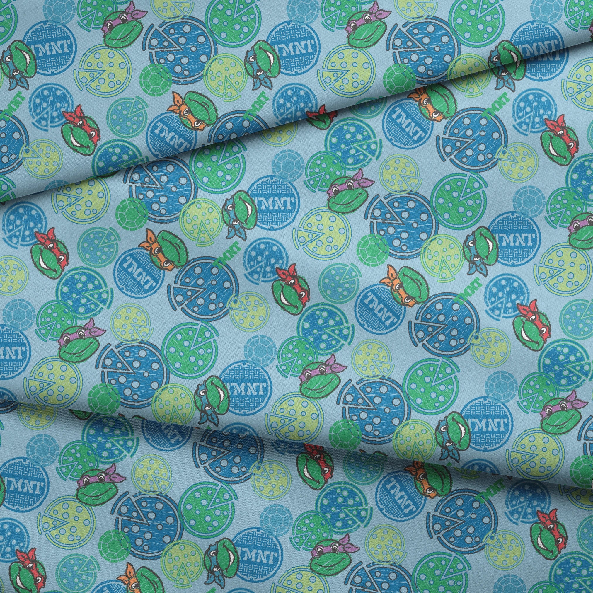 Cartoon Ninja Turtles pattern with colorful circular designs on light blue background fabric fold mockup