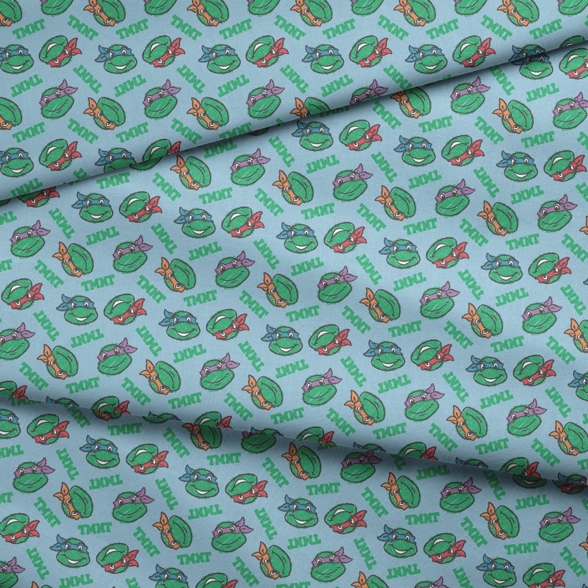 Cartoon pattern of Teenage Mutant Ninja Turtles faces with colored masks on light blue background fabric fold mockup