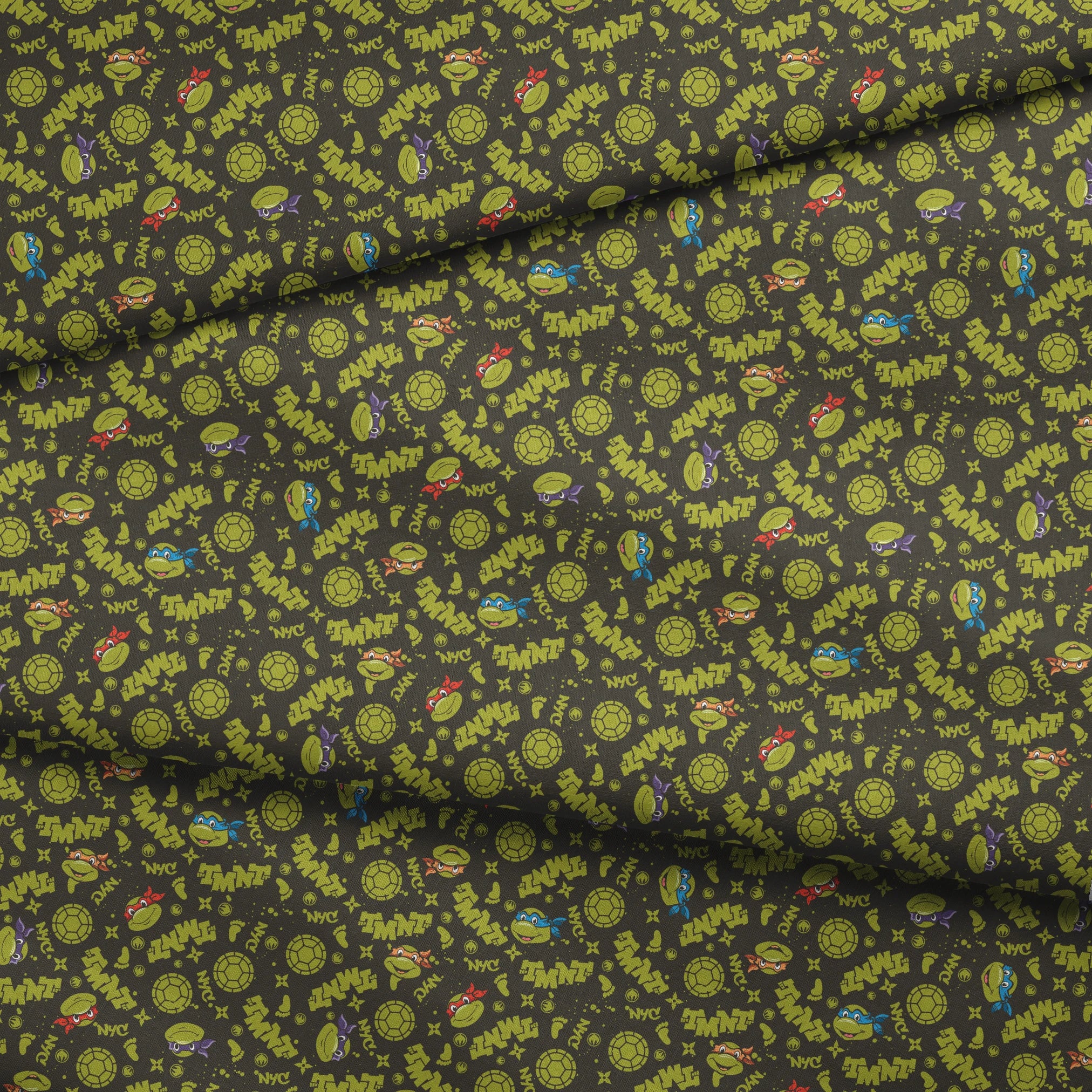 Pattern of Teenage Mutant Ninja Turtles with "TMNT" text on dark background fabric fold mockup