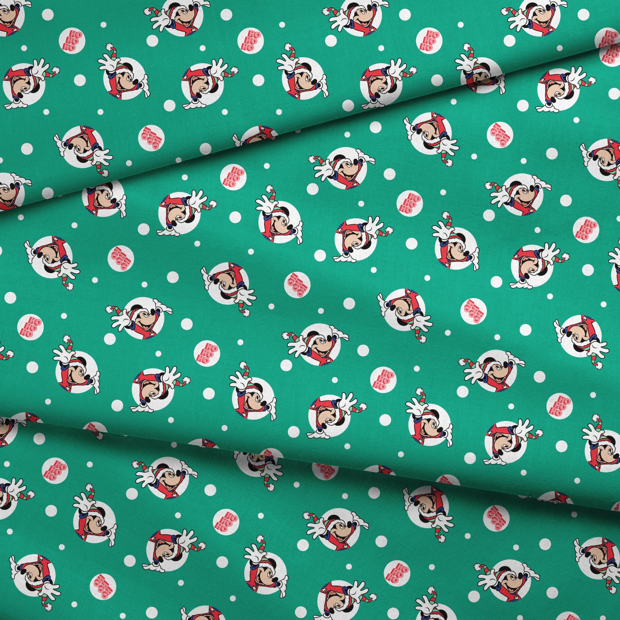 Mickey Mouse in Santa hats on green polka dot background with "Ho Ho Ho" text fabric fold mockup