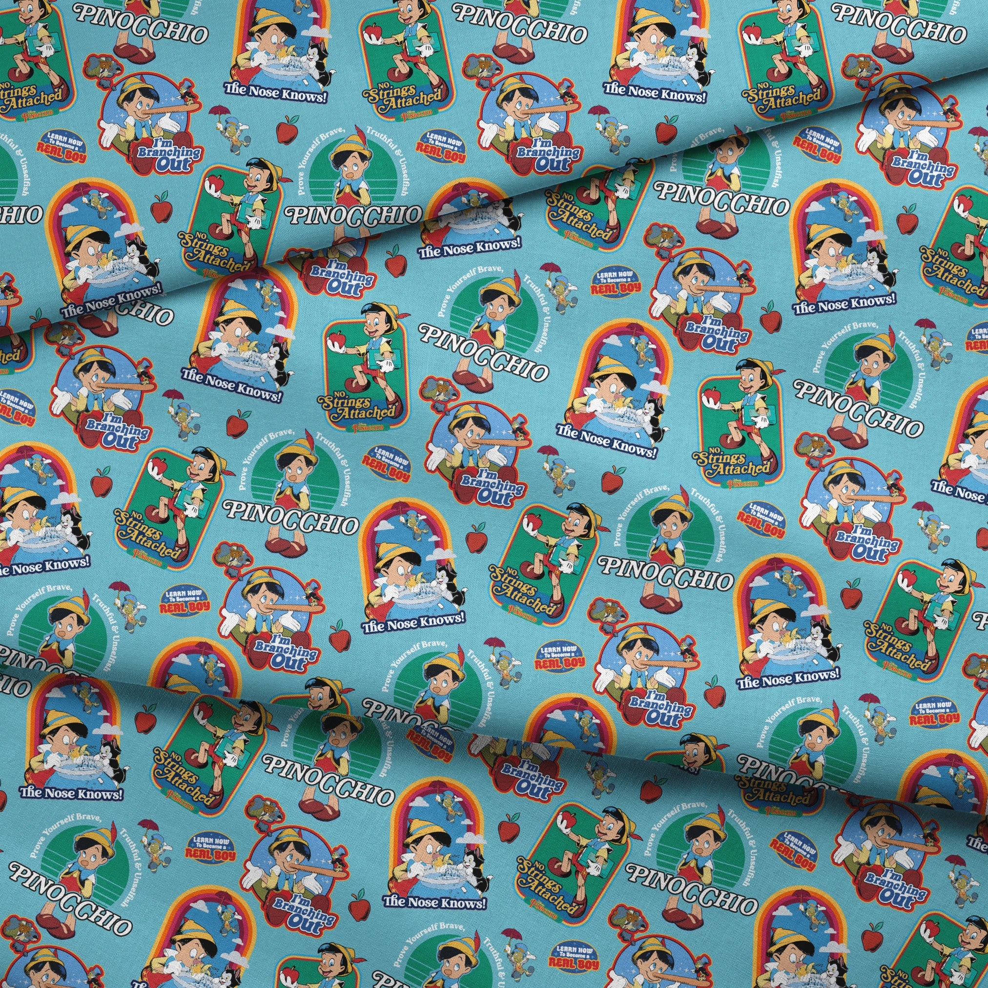 Colorful Pinocchio cartoon pattern featuring puppet characters, slogans, and red apples on teal background fabric fold mockup