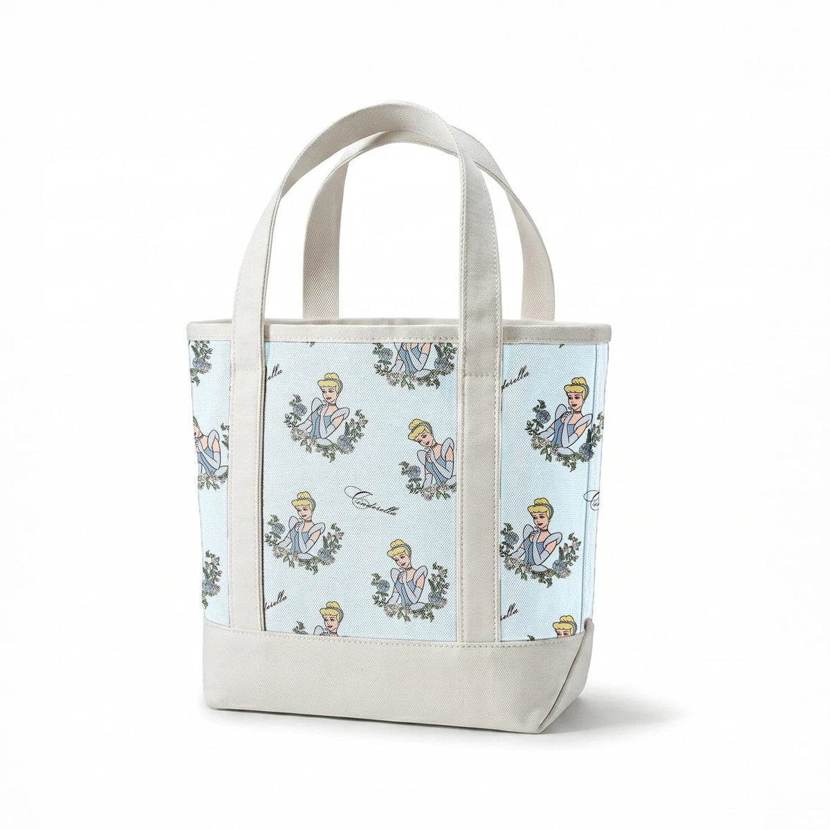 The image shows a pattern featuring a cartoon princess character in a blue dress surrounded by decorative green wreaths on a light blue background. The word "Cinderella" appears in cursive script throughout the design. springs canvastote mockup