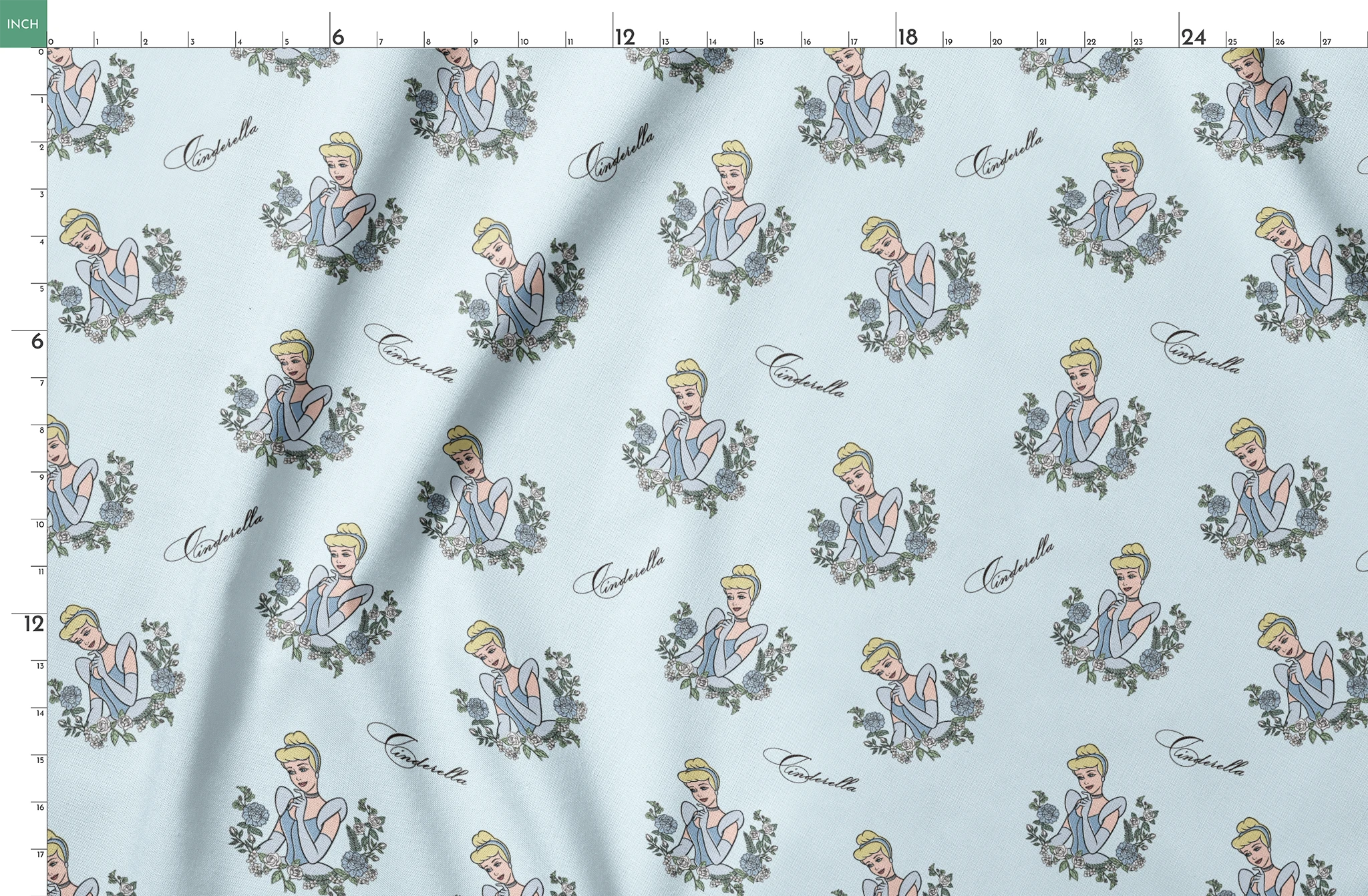 The image shows a pattern featuring a cartoon princess character in a blue dress surrounded by decorative green wreaths on a light blue background. The word "Cinderella" appears in cursive script throughout the design. springs fatquarter mockup