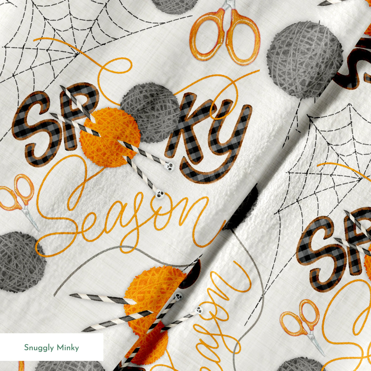 Halloween design by Nicole Tamarin featuring orange and gray yarn balls, scissors, spiderwebs, and “Spooky Season” lettering on a cream background. springs minky texture