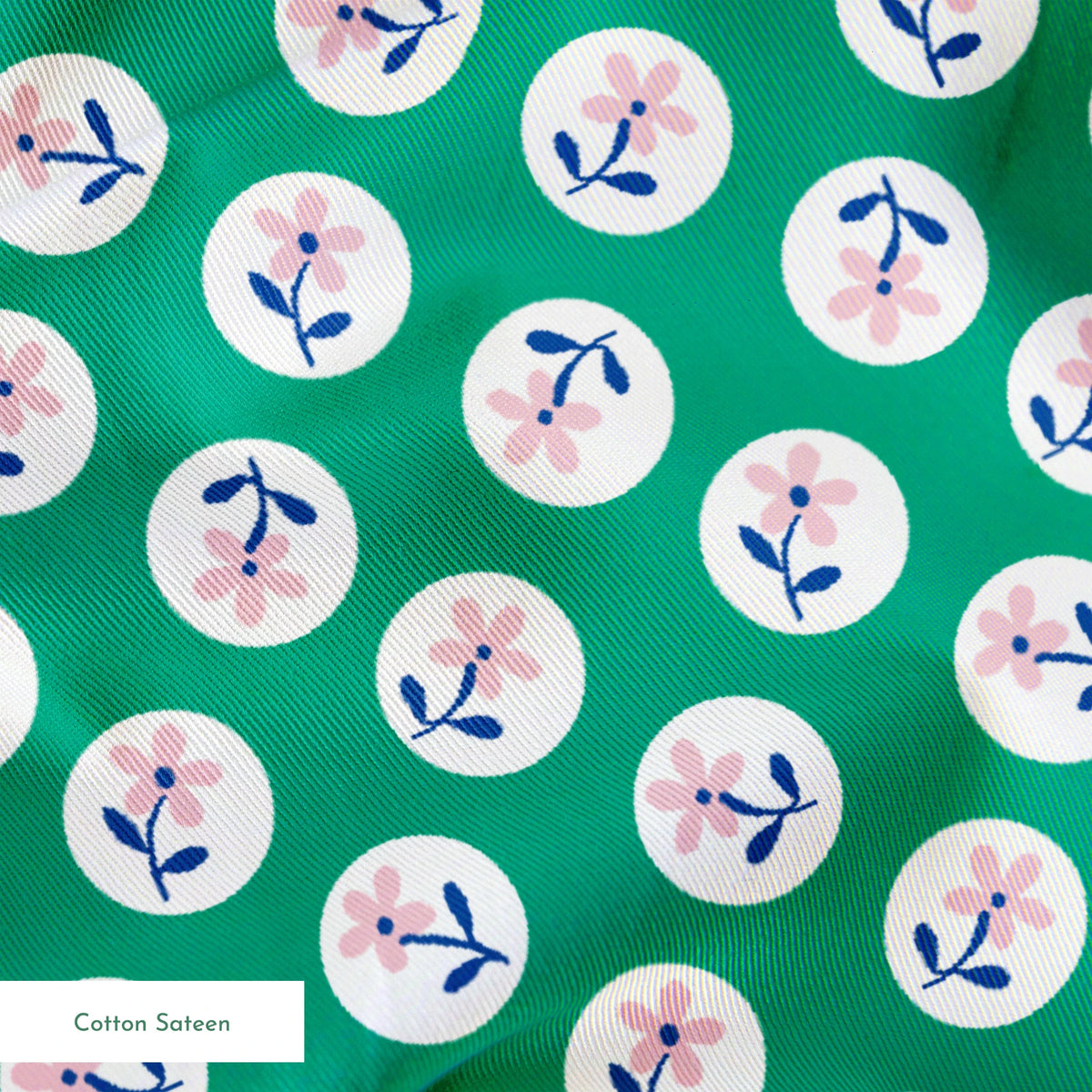 Pink flower motifs with blue stems on white circles against a green background springs sateen texture