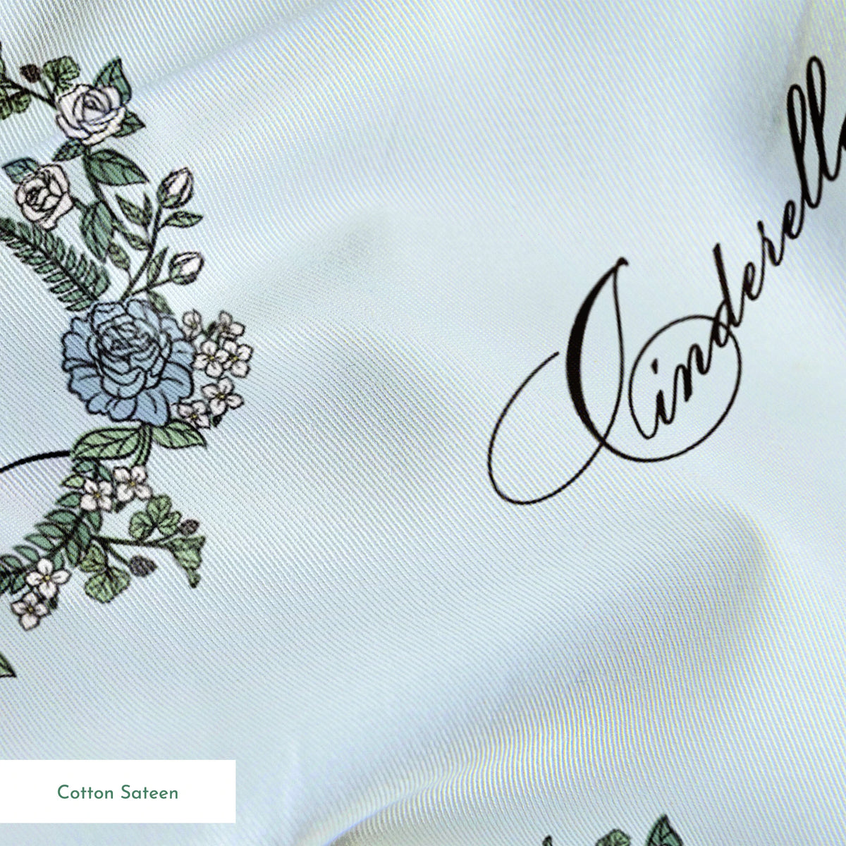 The image shows a pattern featuring a cartoon princess character in a blue dress surrounded by decorative green wreaths on a light blue background. The word "Cinderella" appears in cursive script throughout the design. springs sateen texture